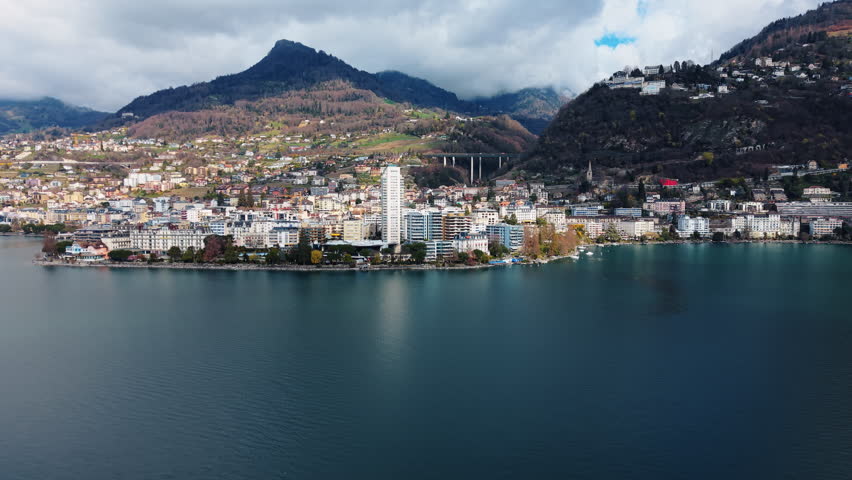 Aerial: Lake Geneva, Montreux cityscape and mountains during the day in Canton of Vaud, Switzerland, orbit drone shot