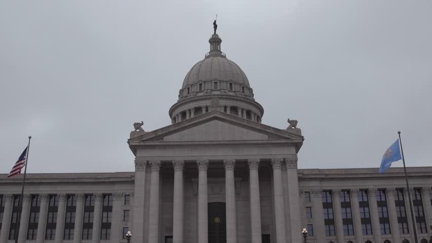 Oklahoma state capitol building exterior view with american and state flags waving on cloudy day