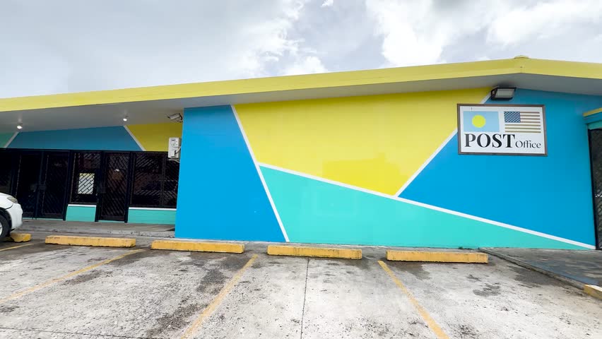 Static wide shot of a bright yellow and blue government post office building in Palau