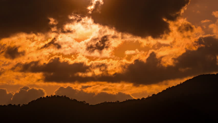 Time-lapse of the sun disappearing behind dark mountain silhouettes under a majestic sky.