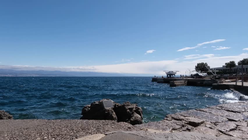 Waves crashing softly on the Adriatic Sea coastline in Lovran, Croatia. Real time blue water splashing on the beach on a windy sunny spring day. Continuous motion of the sea surface with copy space.