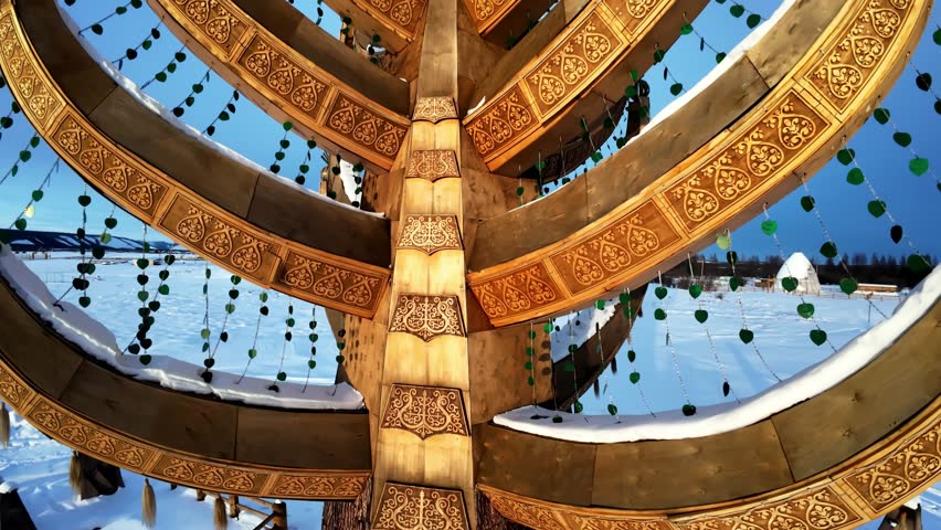 A golden tree-like sculpture with curved branches stands outdoors in a snowy landscape under a clear blue sky.