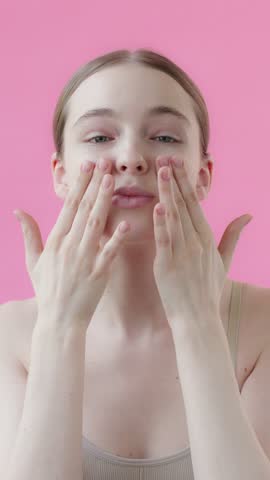Vertical Video: Young Beautiful Woman Posing Looking at Camera Smiling Touching Smooth Face Skin, Skincare on Pink Background in Studio.
