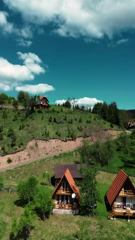 Drone view of wooden cabins on a hillside in Tara National Park, Serbia, during springtime with clear skies and green meadows. Vertical 4k footage.