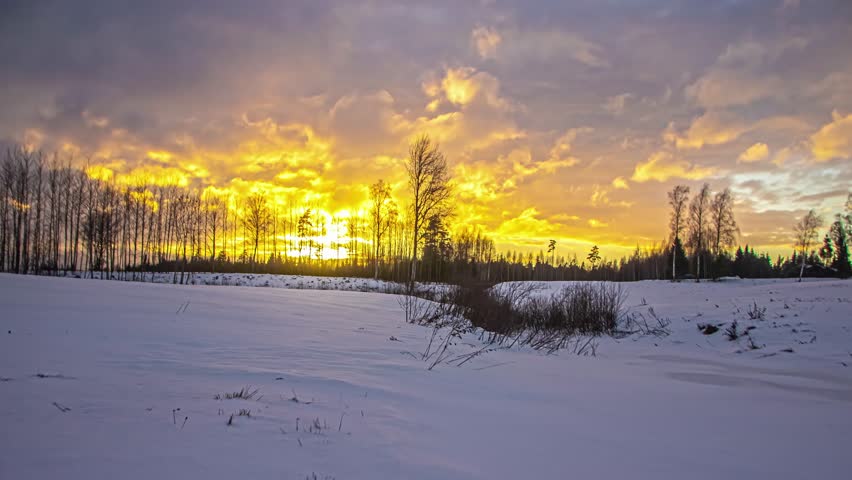 Winter landscape sunset time lapse with colorful sky moving clouds and snow field over forest horizon