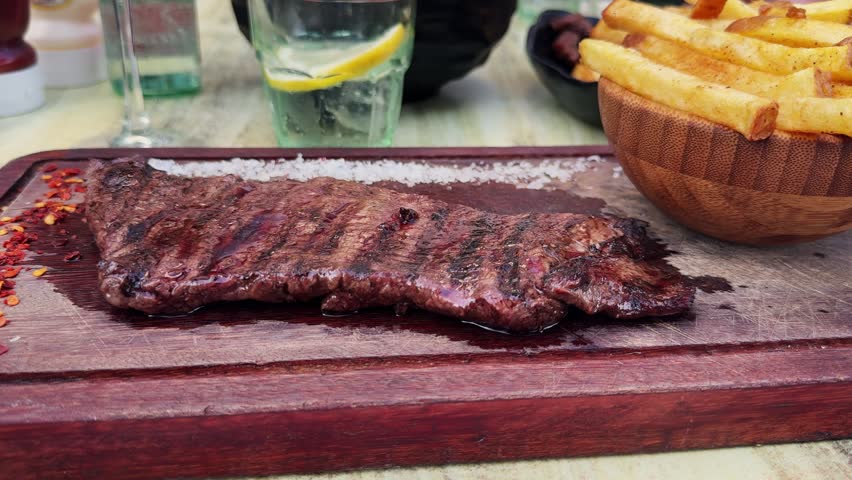 Skirt steak with French fries, coarse salt and pepper on a wooden board served in an Argentine restaurant. High quality 4k footage