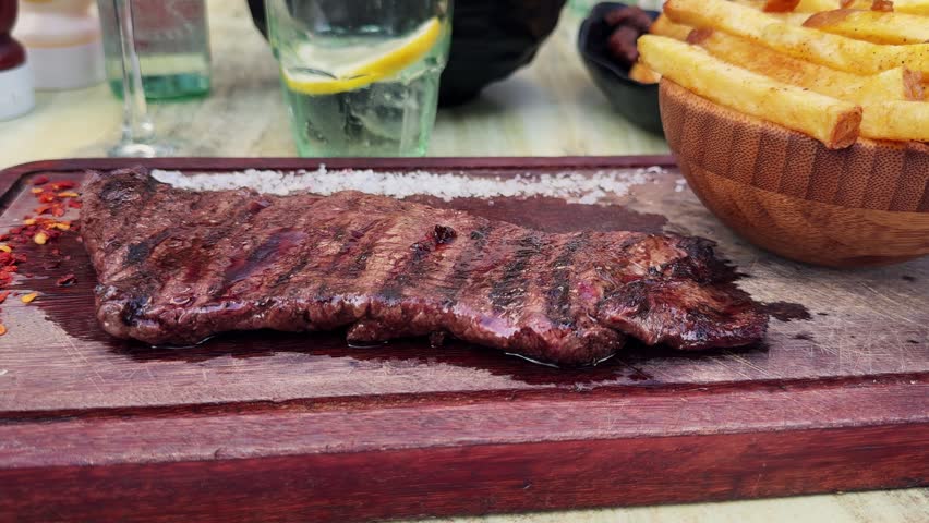 Skirt steak with French fries, coarse salt and pepper on a wooden board served in an Argentine restaurant. High quality 4k footage