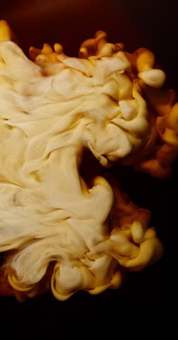 Extreme super slow motion of milk swirling and mixing into coffee, creating smooth creamy clouds and fluid abstract shapes in a dark liquid background. Speed ramp effect. Vertical aspect ratio.