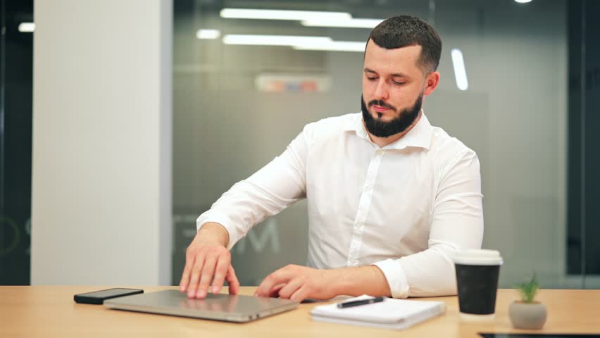Dedicated professional opens laptop, diligently typing at office desk. Concentrated and productive, engaged in remote work. Focused expression conveys seriousness toward tasks.