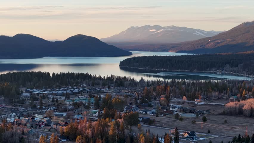 Scenic aerial view of Whitefish, Montana near Glacier National Park, showing Flathead River and rugged Rocky Mountains with a serene lake and town at sunset.