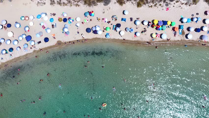 Aerial overhead view of a crowded beach with turquoise sea as seen in Messinia, Greece, during summer time