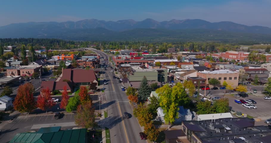 Downtown Whitefish Montana with streets buildings and distant mountain range under clear daylight, aerial medium establish