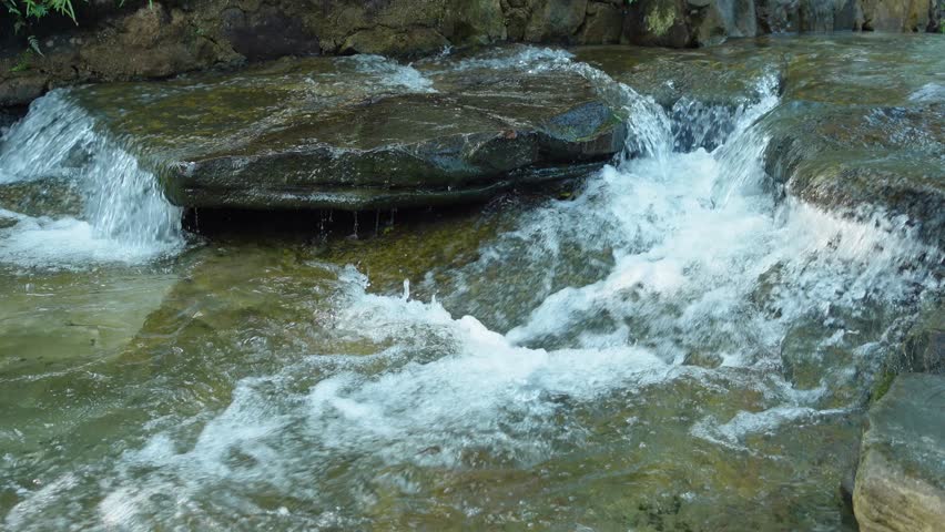 Clear stream water rushing over flat rocks in a small cascade, capturing natural movement, fresh flow, and tranquil outdoor scenery in a rocky creek setting.