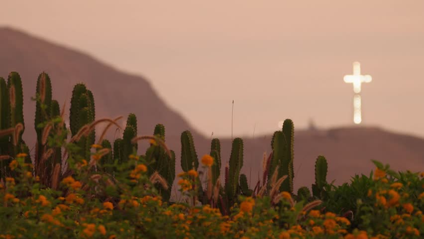 Scenic pan of Barranco Park, Lima, at sunset. The iconic illuminated Chorrillos Cross stands in the background under golden hour light, showcasing Peru