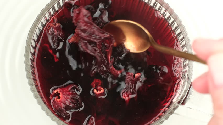 Woman stirs hot hibiscus tea in cap closeup. Cooking homemade healthy organic red hibiscus tea