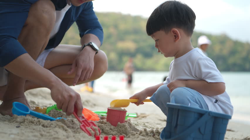 A little child enjoying sand play on the beach during a holiday, with their father playing beside them
