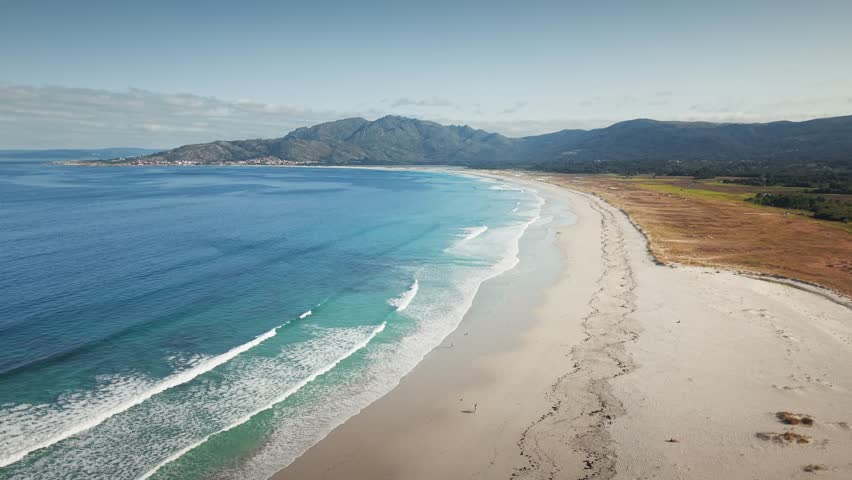 Drone pullback over Praia da Carnota revealing Atlantic waves, sandy shoreline and Monte Pindo mountains in Galicia, Spain.