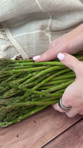 Hands gently arrange fresh asparagus on wooden surface with linen background
