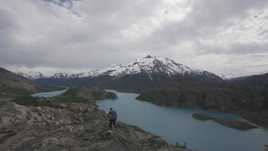 Man standing at a viewpoint overlooking Lake Belgrano and snow capped mountains in nature. Patagonia, Argentina