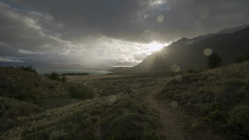Silhouette of a hiker walking on a trail toward a lake during sunset in nature