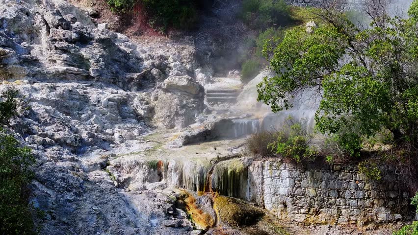Aerial view of Furnas fumaroles where steam rises from geothermal vents, surrounded by dark rocks and contrasting volcanic textures in the Azores, Portugal.