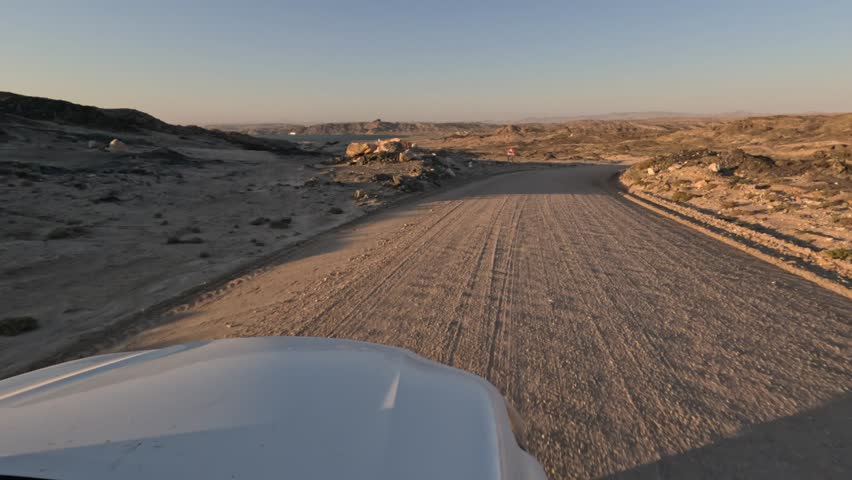 White car drives along a dusty road in the Namibian mountains, southern Namibia, Africa.