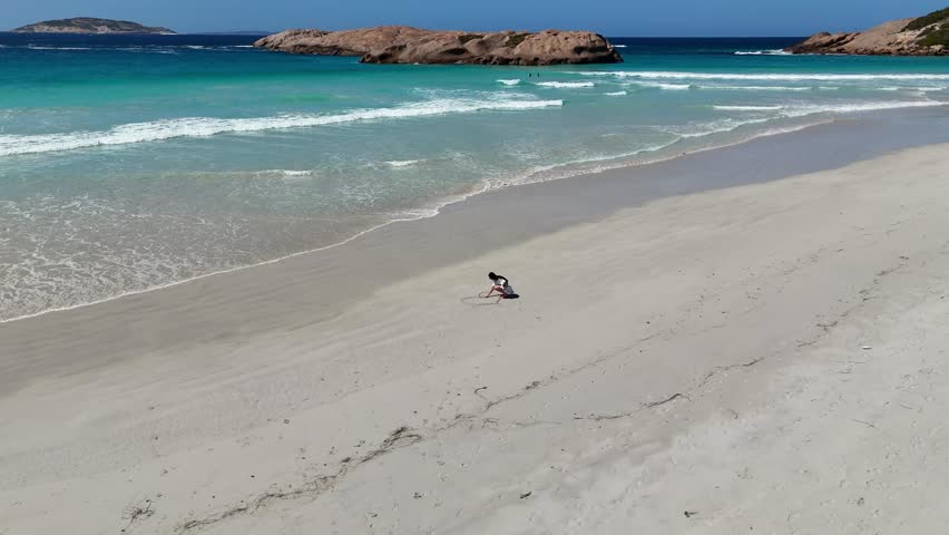Aerial drone view of Twilight Beach in Esperance, Western Australia. Stunning views of white sandy beaches, turquoise waters, and a dramatic granite coastline, with a girl drawing a heart in the sand.