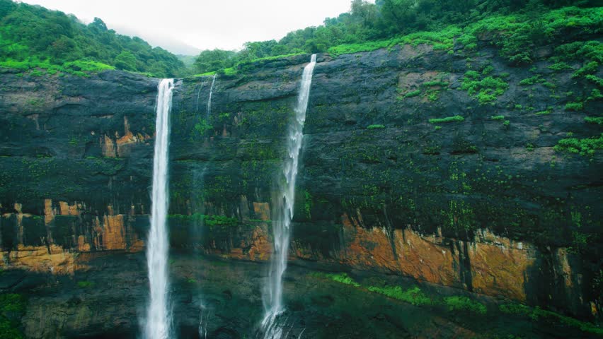 4K Aerial view of majestic Kataldhaar waterfall flowing from cliff during rainy day in Sahyadri Hills, Maharashtra, India. Green trees in forest hill and waterfall flowing in valley. Nature monsoon landscape. Travel background.