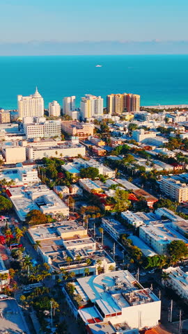 Urban buildings leading to a sandy beach and turquoise ocean under a clear sky. Aerial cityscape of coastal town with beach and hotels. Miami Beach. Vertical video.