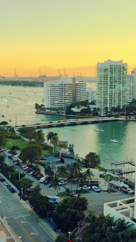 Waterfront park, parking lot, and a bridge with car traffic during evening. Aerial view of Miami Beach and bridge at dusk. Vertical video.