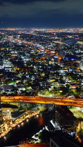 Miami river at night with glowing highway bridge, illuminated buildings, and city skyline under cloudy sky. Night aerial panorama of city highway. Vertical video.