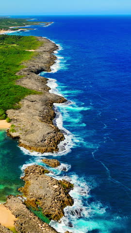 Long perspective of a jagged rocky coast with crashing waves and deep blue atlantic water. Aerial view of rocky shoreline and blue ocean in Puerto Rico. Vertical video.