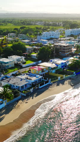 Residential buildings along the coastline with ocean waves hitting the sand. Aerial view of beachfront houses and sandy shore Puerto Rico. Vertical video.