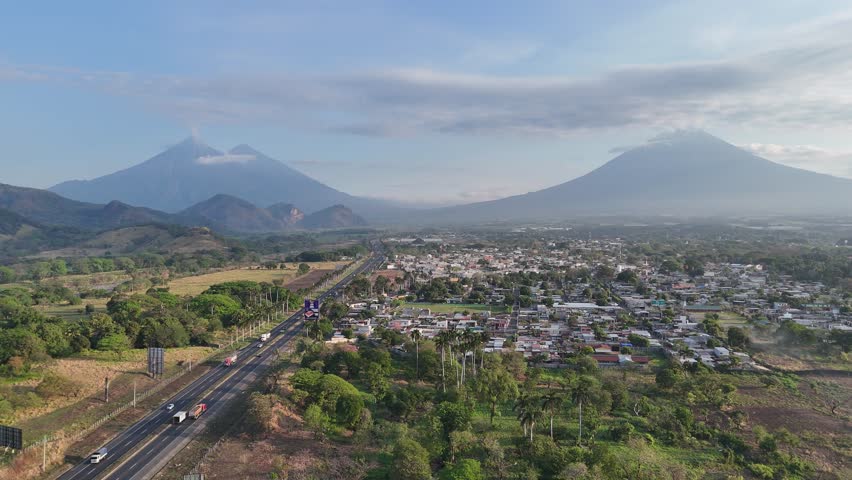 Aerial view of highway from Escuintla to Guatemala with Agua, Acatenango and Fuego volcanoes, Fuego erupting, static drone shot, scenic landscape in Central America