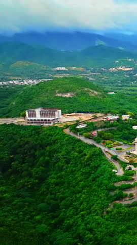 High angle view of a white building and a large cross monument on a lush green hillside with mountains in the distance. Aerial view of mountain landscape with hotel. Puerto Rico. Vertical video.