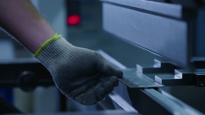 Worker hand guiding metal sheet into press brake machine in industrial factory workshop.