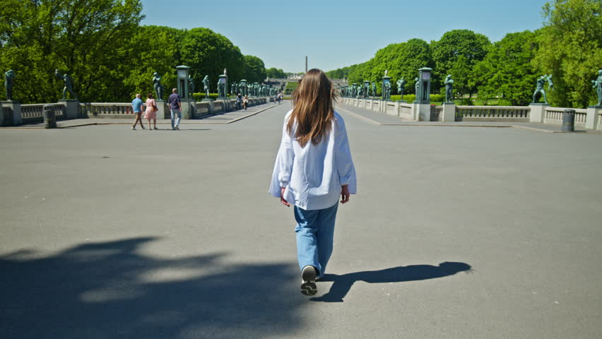 Tourist woman walking across the wide stone plaza in Vigeland Sculpture Park in Oslo. Spacious square and green trees during summer Frogner Park, Norway.