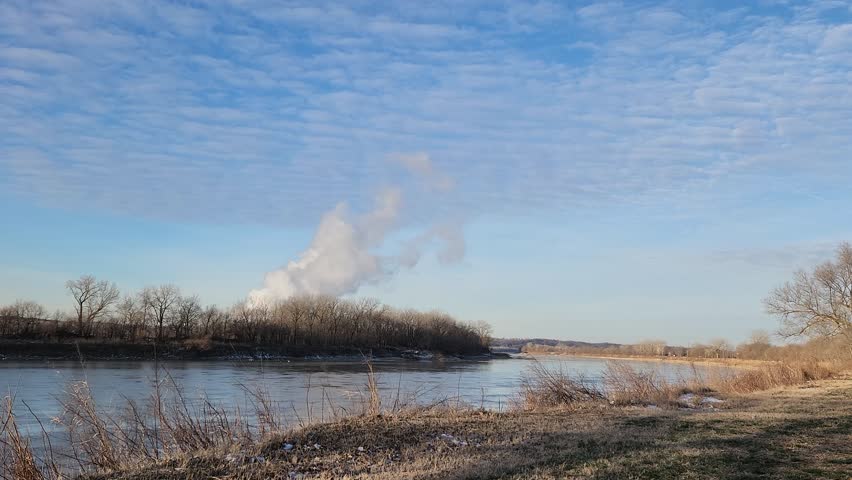 Winter river landscape with drifting steam plume and textured cloud sky, natural motion and open composition
