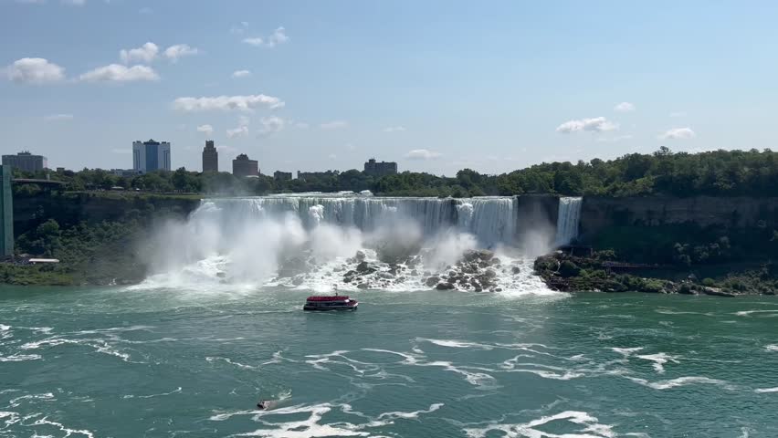 This 4K video captures Niagara Falls on the border of Ontario, Canada, and New York, USA. The visual documents the Horseshoe, American, and Bridal Veil Falls with a tourist boat in the river below. The composition illustrates a 168,000 cubic meter flow rate, documenting fluvial geomorphology and hydroelectric resources for nature, travel, and editorial media.