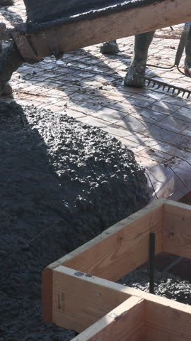 Workers are pouring fresh concrete into wooden forms at construction site, ensuring solid foundation.