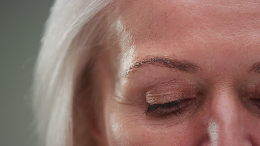 Close up portrait: old eye female, macro. Beauty senior woman with grey hair open eyes. Retired lady looks up, wrinkles skin. Eyesight or vision. Grandma lifts her eyelids, looking and blinking