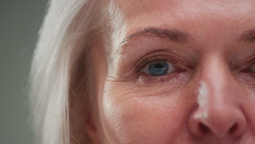 Close up portrait: old eye female, macro. Beauty senior woman with grey hair open eyes. Retired lady looks up, wrinkles skin. Eyesight or vision. Grandma lifts her eyelids, looking and blinking