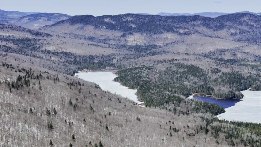 Aerial view of frozen lake in Quebec with forest and mountains under blue sky. g.