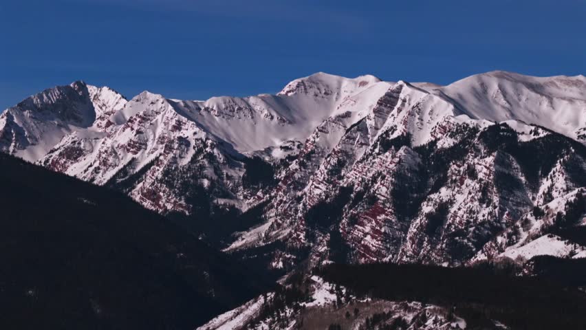 Maroon Bells Wilderness prominent peaks Aspen Snowmass valley aerial drone Colorado landscape winter spring sunny early morning blue sky Elk Range Rocky Mountains circle right motion