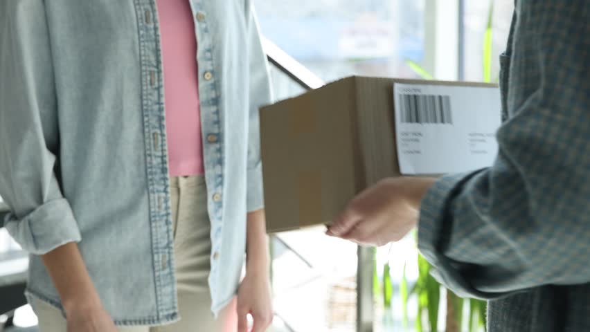 Parcel delivery. Post office worker giving cardboard box to woman indoors, closeup
