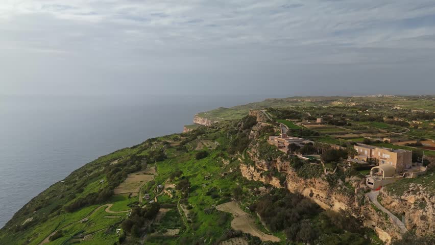 Dingli Cliffs, Malta, feature dramatic limestone cliffs overlooking the Mediterranean Sea, with terraced fields, rural countryside, and stone buildings visible in this elevated orbital aerial view.