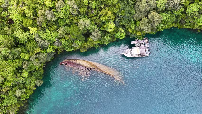 High angle drone shot captures a sunken shipwreck in turquoise water beside lush green islands