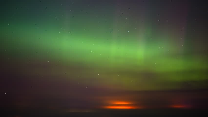 Dramatic drone time lapse featuring glowing green northern lights swirling in night sky above snowy mountain landscape and distant horizon representing natural wonder and celestial light show