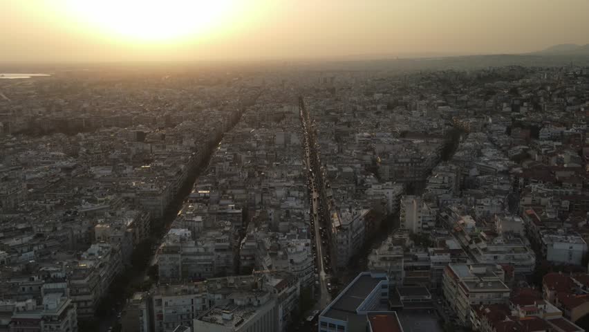 Sweeping aerial shot of thessaloniki city, greece, showing dense buildings and streets at sunset