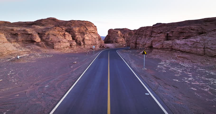 Aerial view of winding asphalt road through rock canyon at dusk, Xinjiang, China. 